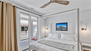 A modern bedroom with a large bed, a ceiling fan, and a balcony with a view.
