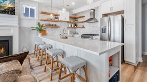A modern kitchen with white cabinetry, a central island with bar stools, and a stainless steel refrigerator.
