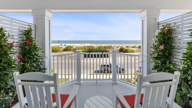 A covered outdoor area with white railings, two white chairs with red cushions, and a view of the beach and ocean.