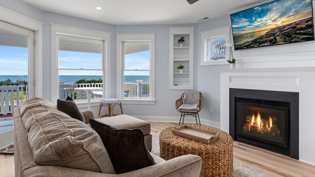 A living room with a fireplace, a sofa, a chair, and a view of the ocean.