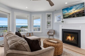 Una sala de estar con chimenea, un sofá, un sillón y vista al océano.