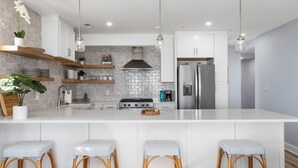 A modern kitchen with a large island, white cabinetry, and hanging pendant lights.