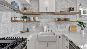 A modern kitchen with white cabinets, grey tiled backsplash, wooden shelves, and a stainless steel range hood.