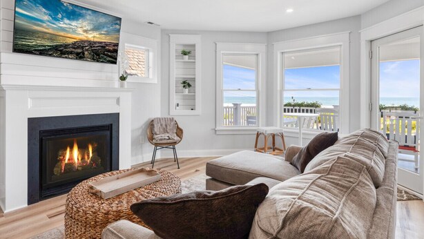 A modern living room with a fireplace, a large window with a view of the ocean, and a ceiling fan.
