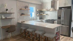 Eine moderne Küche mit Kochinsel, Barhocker, Herd und Kühlschrank.