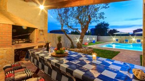 Un patio exterior con un mantel a cuadros, una parrilla y una piscina.