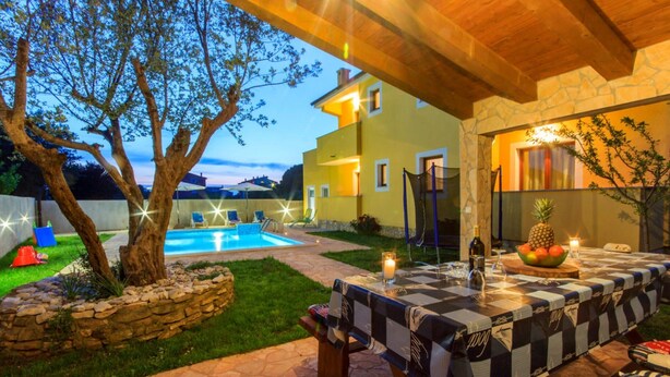 Un área de comedor junto a la piscina con mantel a cuadros, asientos exteriores y una pared de piedra.