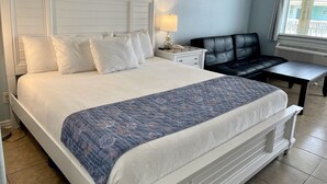 Una habitación de hotel con una cama grande, una mesita de noche, una lámpara, una silla y una ventana con persianas.