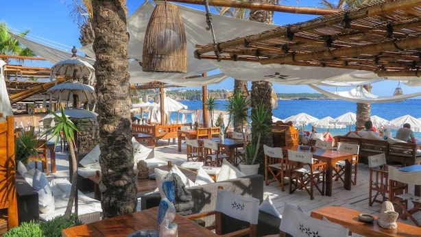 Un espace de restauration en plein air avec des tables et des chaises en bois, des parasols et une vue sur la mer.