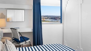 Une chambre d’hôtel comprenant un lit, une chaise, un bureau, un miroir et une fenêtre donnant sur une marina et des immeubles.
