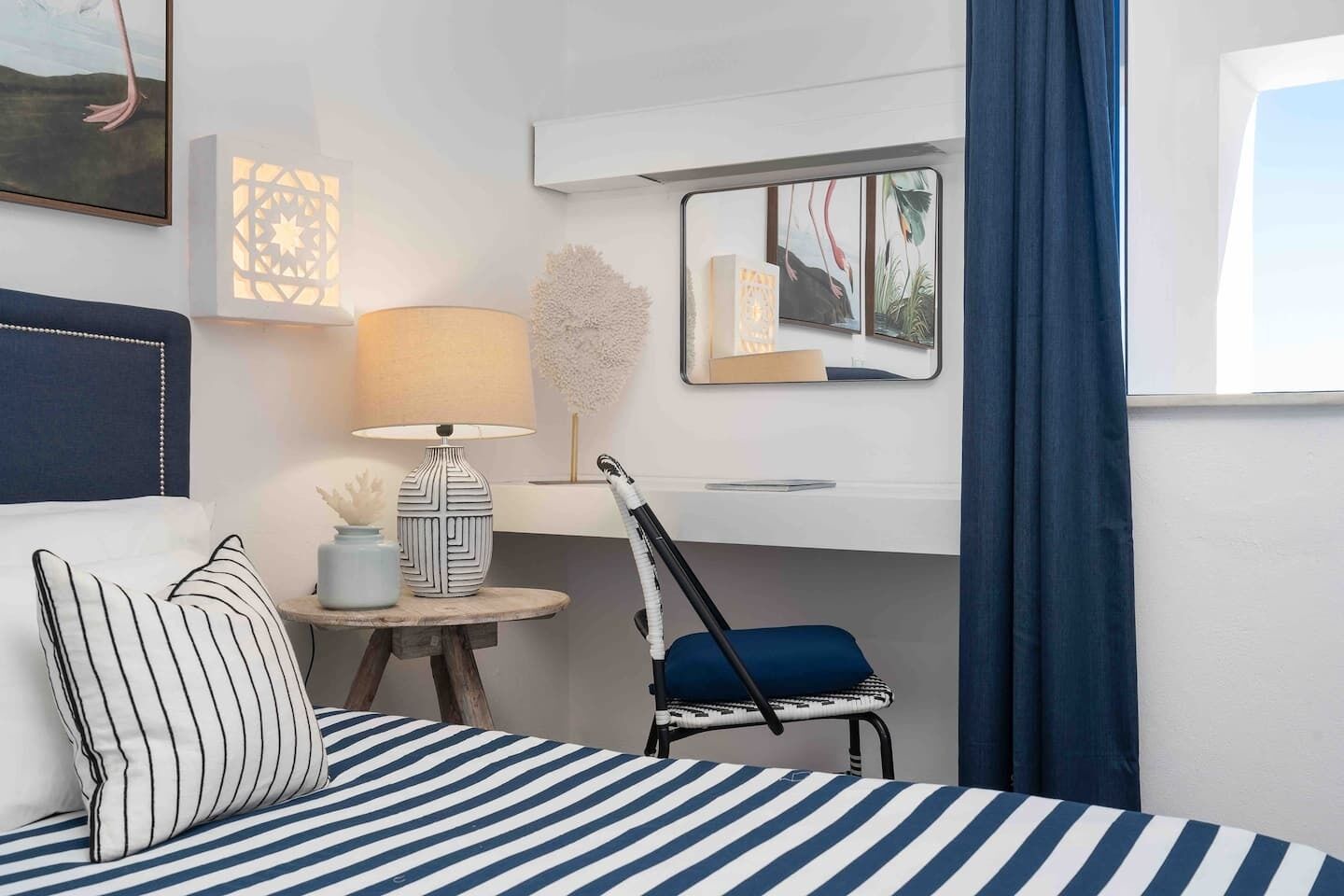 Et hotelværelse med en seng, et skrivebord, en stol, en lampe og et spejl.