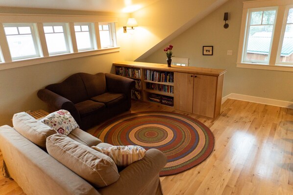 Een gezellige woonkamer met een bruine bank, een beige bank, een houten boekenkast en een kleurrijk vloerkleed.