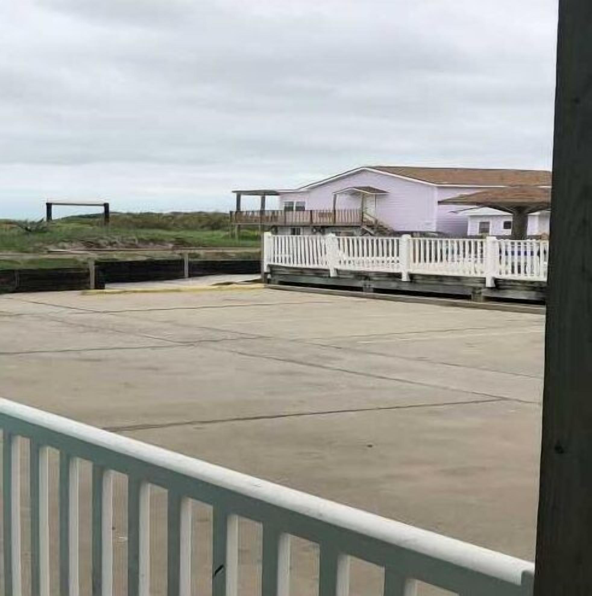 Une propriété située en bord de mer, dotée d’une clôture blanche, d’une terrasse en béton et d’un bâtiment avec un toit en pente.