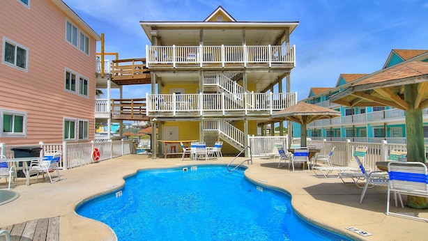 Un hotel de varios pisos con piscina, mobiliario exterior y un puesto de socorrista.