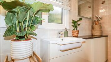 Un baño moderno con un lavabo blanco, un banco de madera y plantas en macetas.
