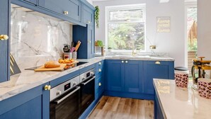 A modern kitchen with blue cabinets, a marble backsplash, and a window with a view of greenery. - Dawns House in the Peaks overlooking the mill pond (Cromford)