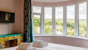 A hotel room with a bed, a TV mounted on the wall, a window with a view of the countryside, and a colorful cabinet. - Dawns House in the Peaks overlooking the mill pond (Cromford)