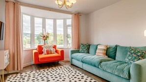 A living room with a bay window, a teal sofa, an orange armchair, and a polka dot rug. - Dawns House in the Peaks overlooking the mill pond (Cromford)
