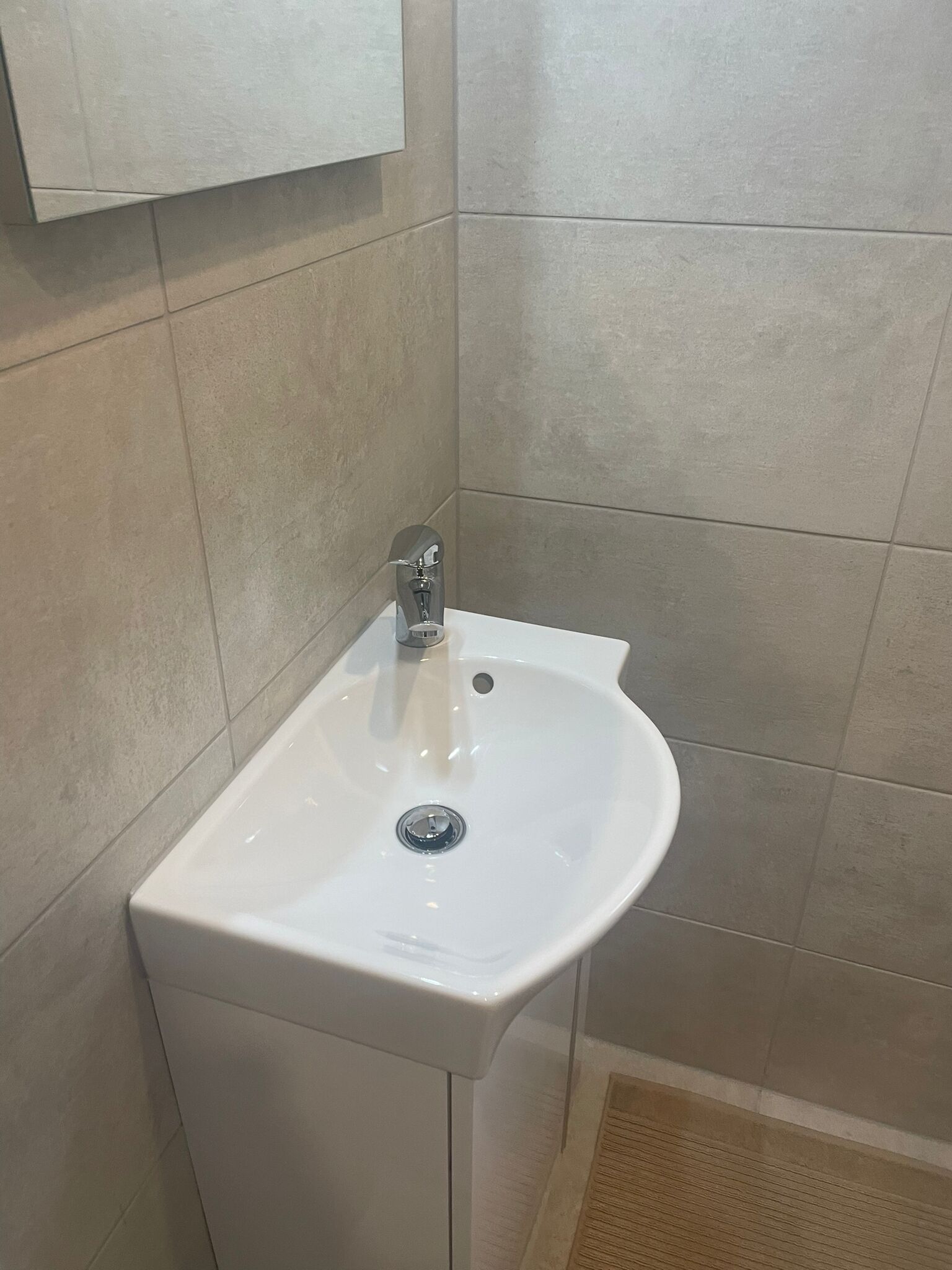 Un baño con un lavamanos blanco, un espejo encima y paredes de baldosas color crema.
