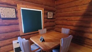 Eine Holzhütte mit einem runden Tisch, vier Stühlen, einem großen Fenster und einem Wandheizgerät.