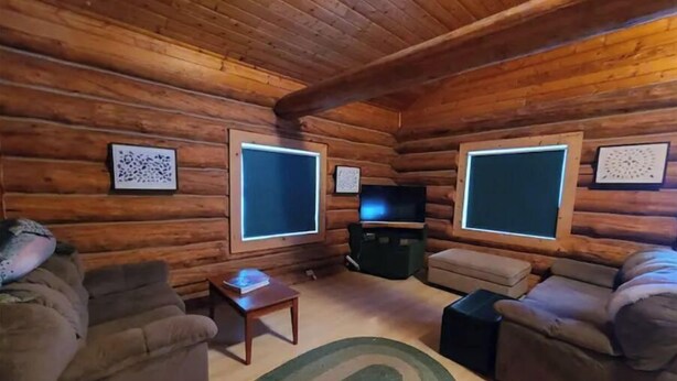 Ein rustikales Blockhaus-Interieur mit zwei Sofas, einem Couchtisch und einem Fernseher.