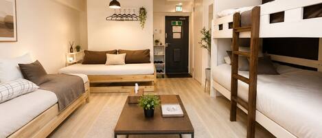 Une pièce moderne et bien éclairée, comprenant un canapé, un lit, un lit superposé et une table basse agrémentée d’une plante.