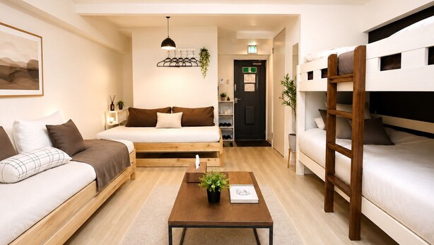 Una habitación moderna y bien iluminada con un sofá, una cama, una pequeña mesa con una planta y una lámpara colgante.