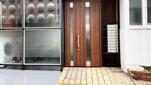 Fachada de edificio con puerta de madera, paneles de vidrio esmerilado y zona de entrada con azulejos.