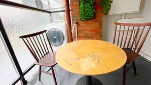 Una mesa redonda con dos sillas de madera, un muro de ladrillo con una planta verde y una lavadora al fondo.