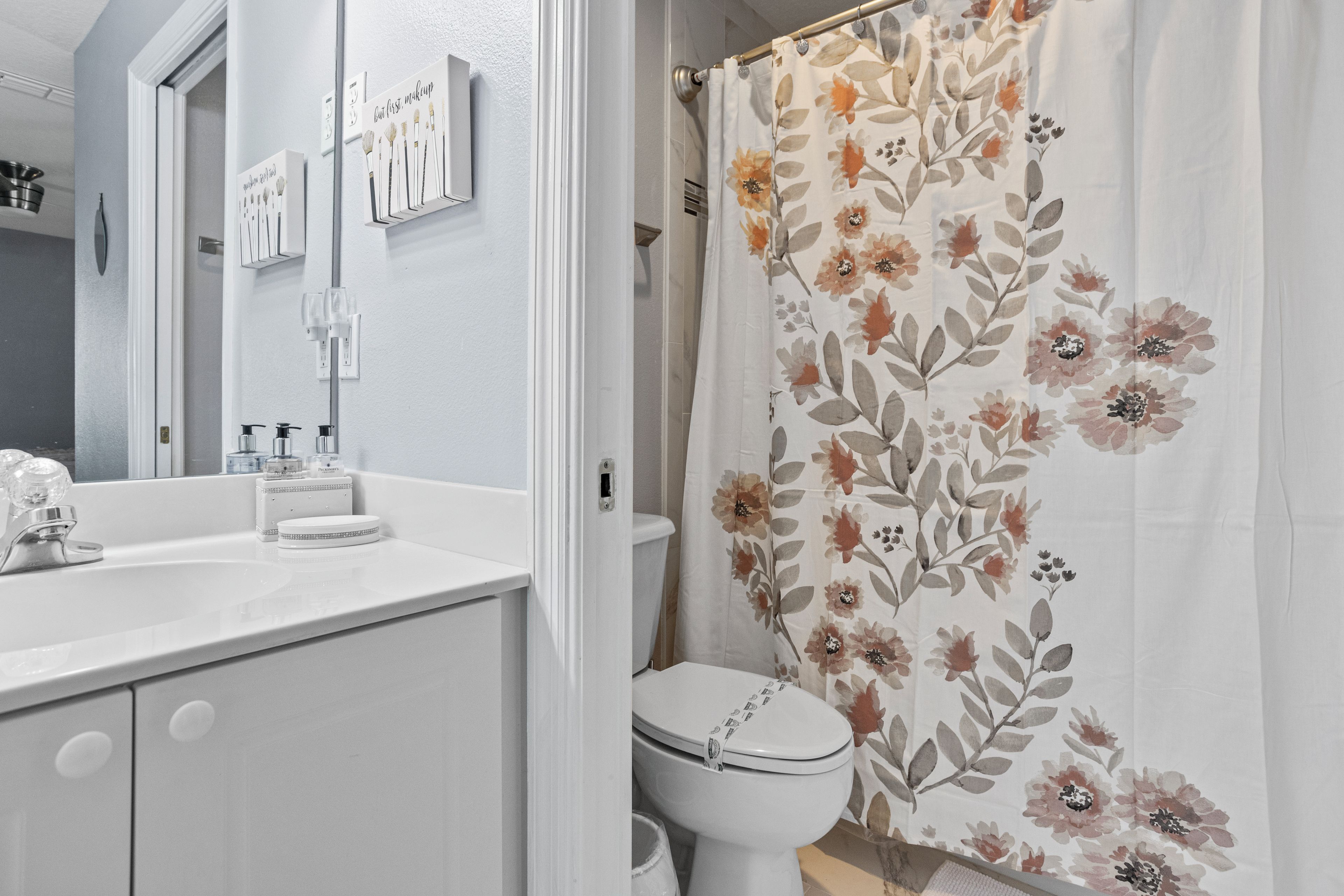 Een badkamer met een wit wastafelmeubel, toilet en douchegordijn met bloemenprint.