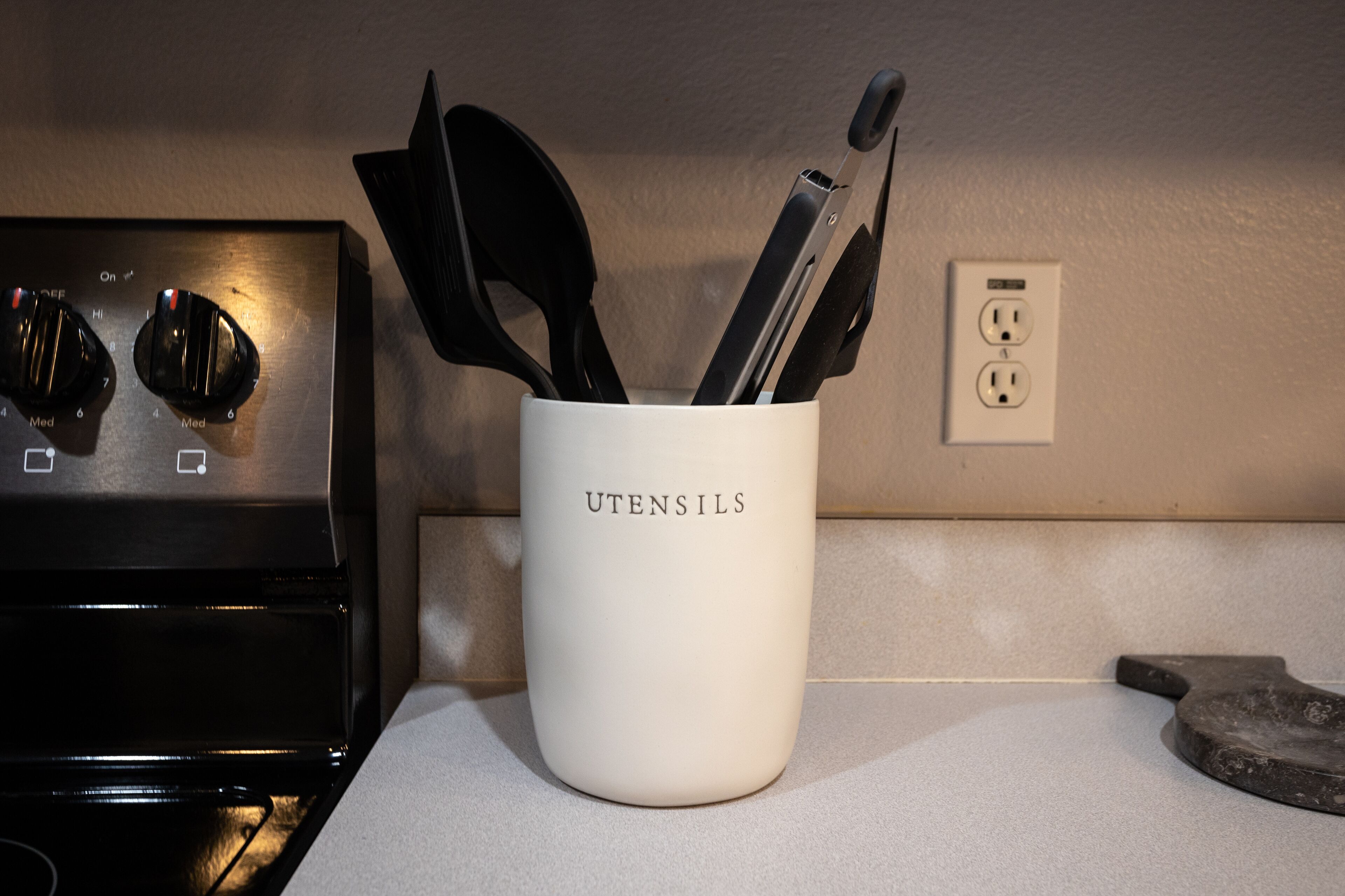 Een keuken met een witte mok met de tekst 'UTENSILS', gevuld met diverse keukengereedschappen.