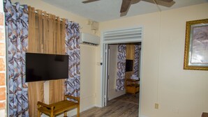 Un salon avec un téléviseur à écran plat fixé au mur, un meuble TV en bois et une table basse en verre.