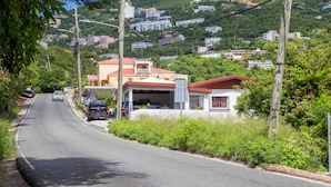 Une route bordée de maisons sur une colline, un garage et des poteaux électriques.