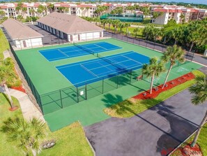 Tenniskenttä, jonka ympärillä on aita, ja taustalla näkyy rakennus.