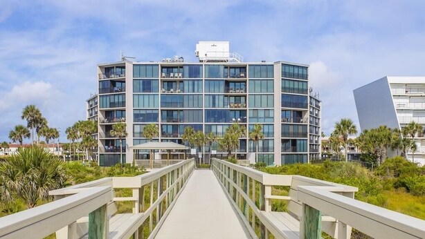 Un hotel moderno con una estructura de varios pisos, un camino de madera que conduce a la entrada y un cielo despejado.