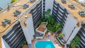 A rooftop pool surrounded by a modern building with multiple floors, outdoor seating, and a landscaped garden area.
