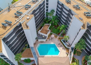 A rooftop pool surrounded by a modern building with multiple floors, outdoor seating, and a landscaped garden area.
