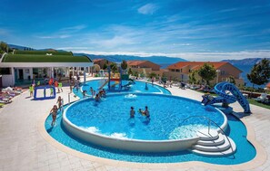 Relax by the central pool, featuring a water slide and a separate children's pool, surrounded by sun loungers and umbrellas.