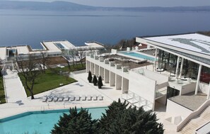 Relax by the infinity pool overlooking a serene body of water, surrounded by sun loungers and a covered seating area.