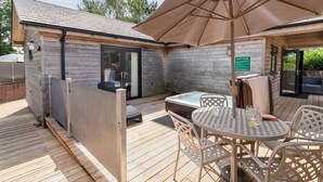 Une terrasse en bois avec un jacuzzi, des sièges d’extérieur et un espace abrité avec un parasol.
