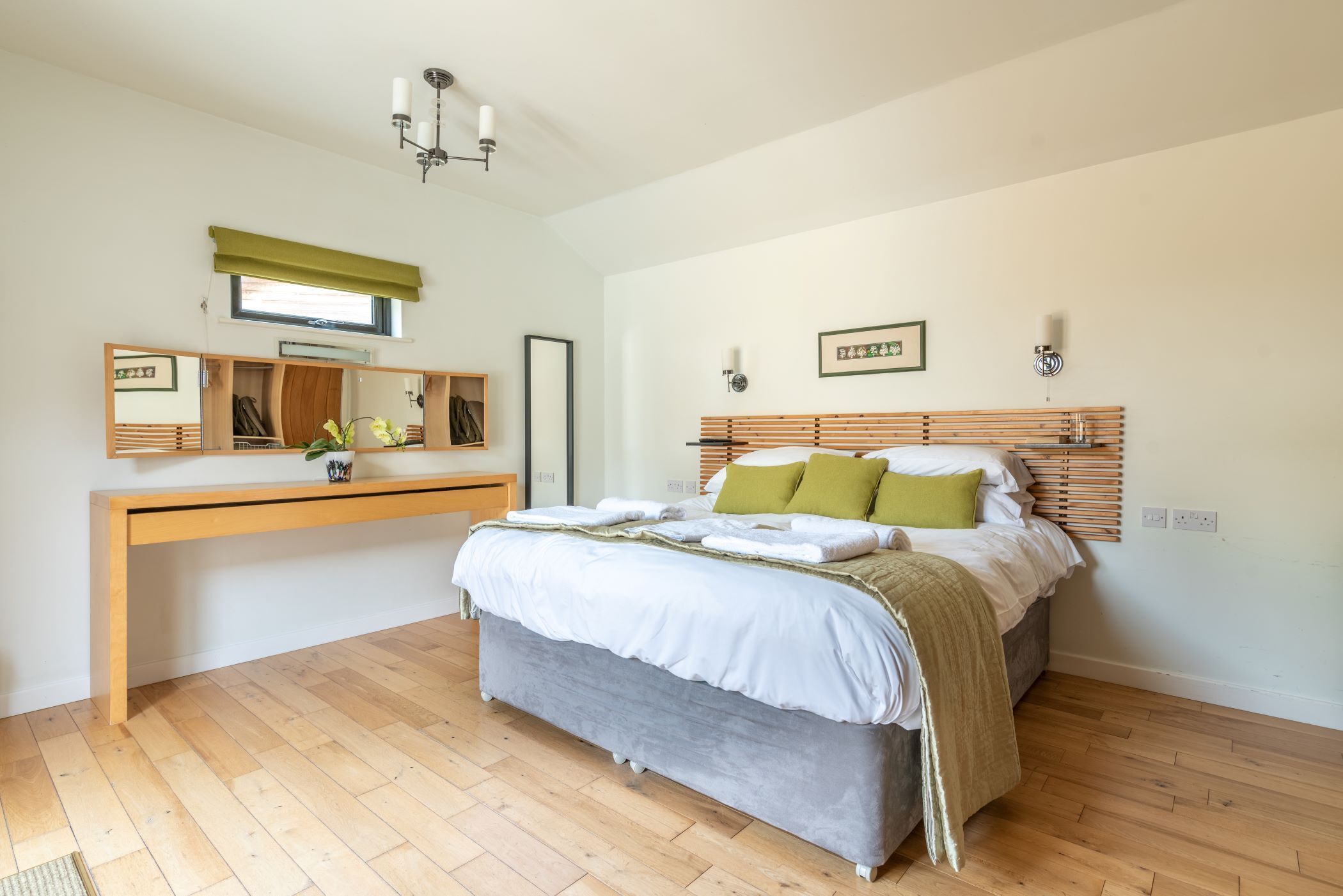 A bedroom with a bed, bedside tables, a mirror, and a window with a green blind.