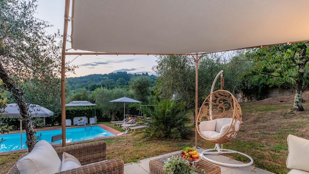 A patio with wicker furniture, a hanging chair, and a pool. - Villa Dondolino in Lucca (Lucca)
