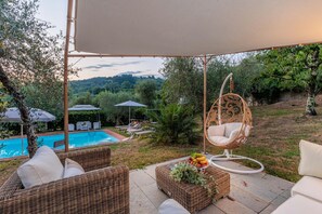 A patio with wicker furniture, a hanging chair, and a pool. - Villa Dondolino in Lucca (Lucca)