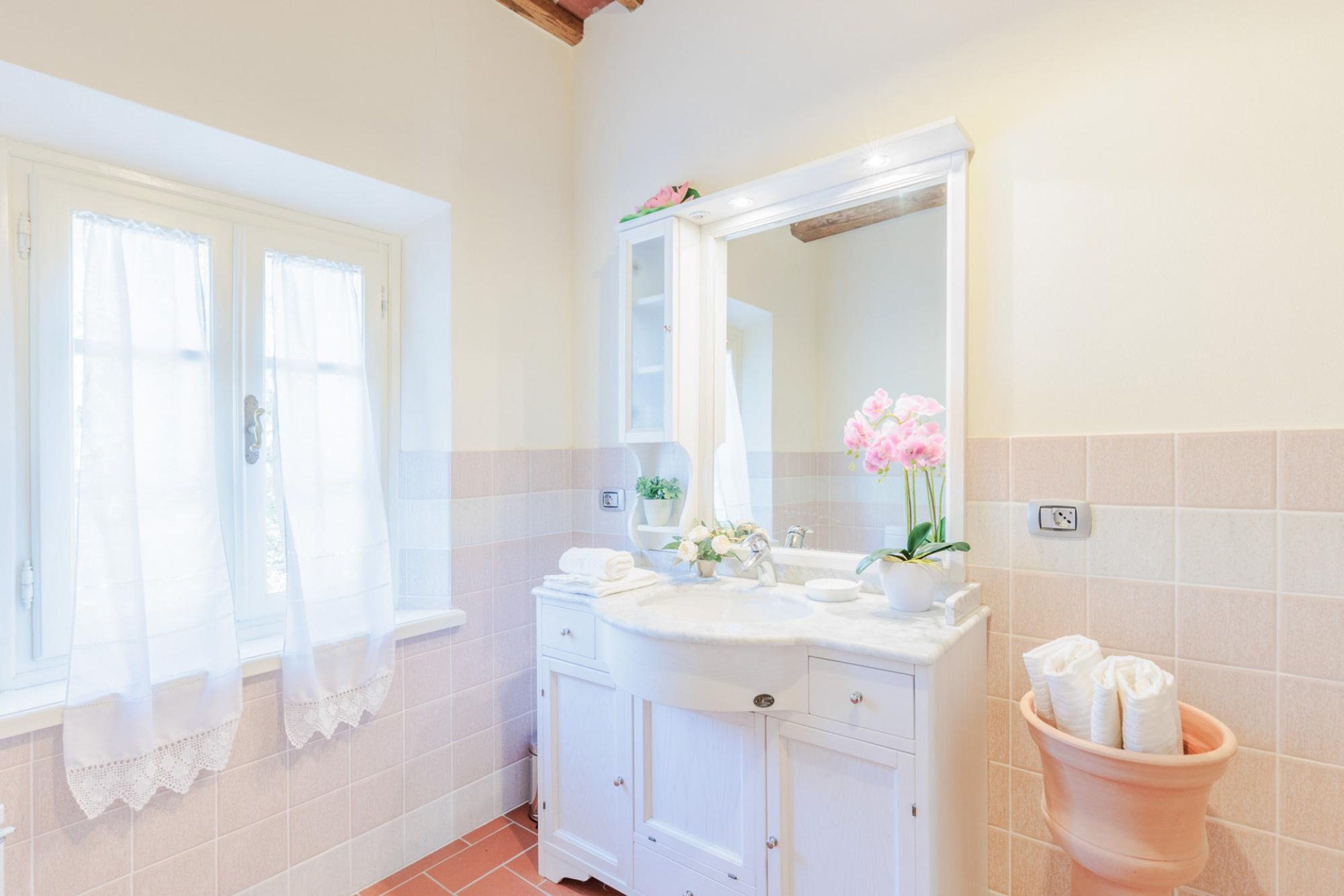Un baño con tocador blanco, espejo y lavamanos de terracota.