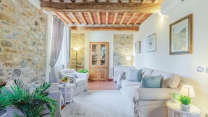 A cozy living room with stone walls, wooden beams, a sofa, a coffee table, and a lamp. - Villa Dondolino in Lucca (Lucca)