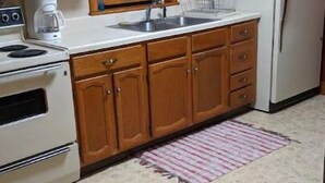Een keuken met houten kastjes, een witte koelkast, een fornuis, een spoelbak en een raam met een witte gordijn.