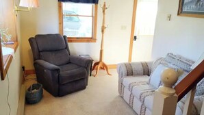 Een woonkamer met een donker fauteuil, een gestreept sofa, een houten gitaar en een lamp.