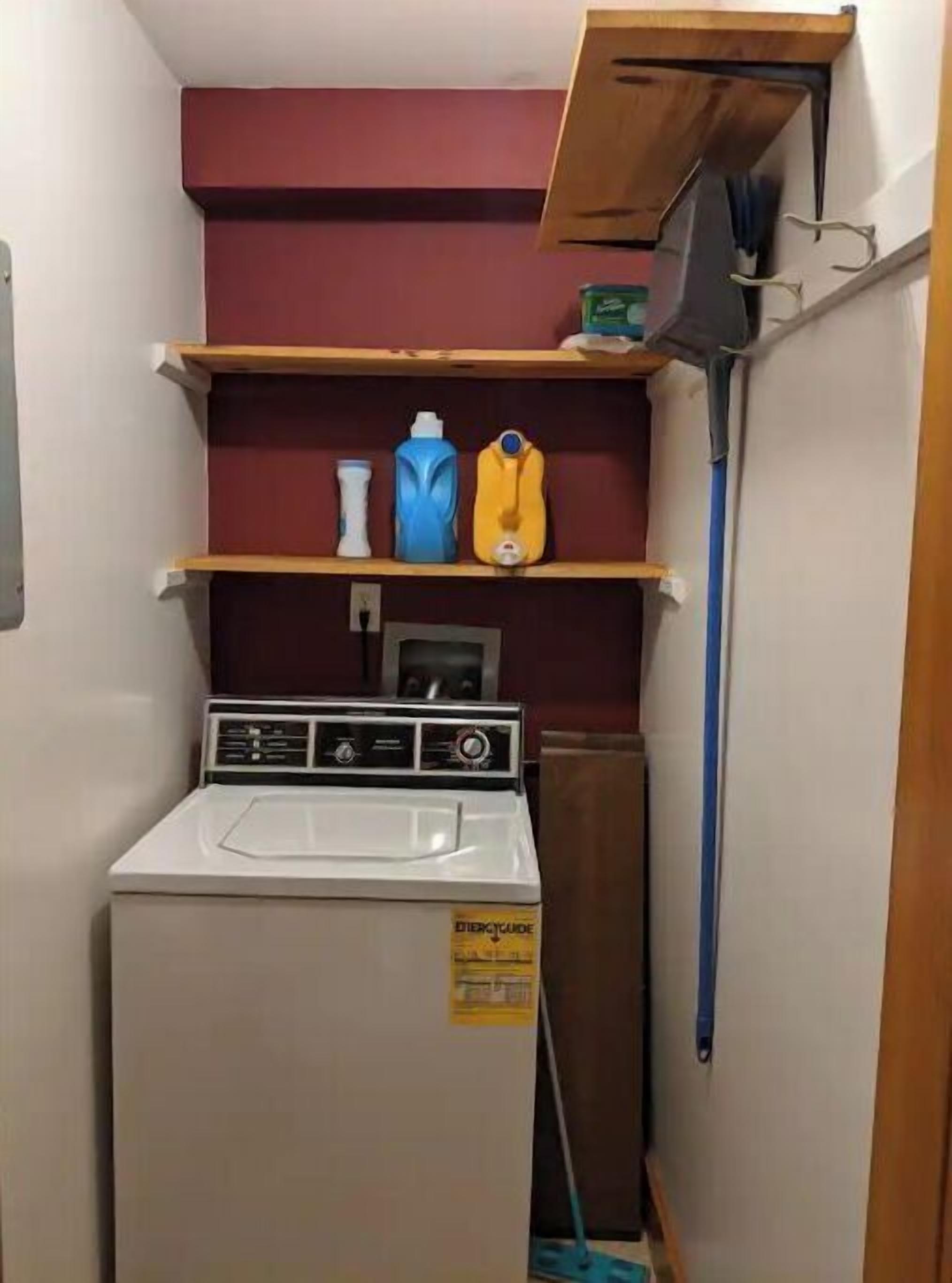 A compact laundry area with a washing machine, shelves with cleaning supplies, and a mop.