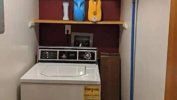 A compact laundry area with a washing machine, shelves with cleaning supplies, and a mop.
