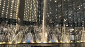 Une vue nocturne d’un hôtel à plusieurs étages, avec une fontaine au premier plan et des fenêtres illuminées.